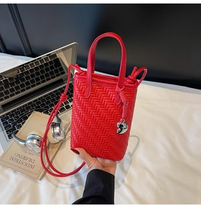 Detail view of red woven crossbody bag with silver heart charm on white minimalist background
