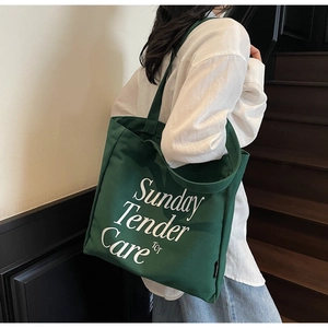 Vista detallada del bolso tote de lona verde oscuro con letras blancas Sunday Tender Care