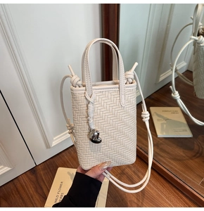 Detail of cream woven leather mini bag featuring silver heart charm and crossbody strap