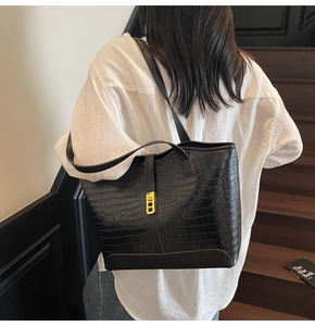 Detail of black crocodile texture tote bag featuring a golden metallic lock closure