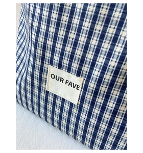 Close-up of blue checkered canvas tote bag with a minimalist stitched logo label