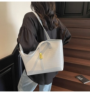 Detail view of large tote bag with crocodile texture and golden clasp on model