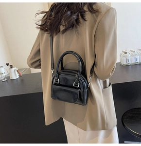 Detail of a black glossy mini handbag with twin top handles and adjustable strap