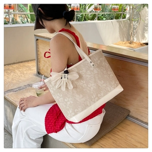 Detail of a beige canvas tote bag with floral prints and a white flower satin charm
