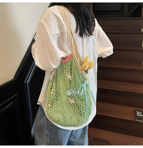 Detail of green crochet tote bag with starfish decor and sea shell charms worn by a model