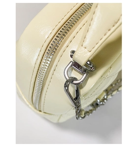 Close-up of silver metal zipper and quilted leather detail on cream shoulder bag