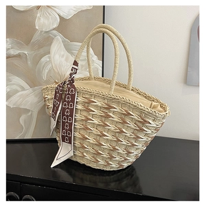 Detailed view of woven straw tote bag handles with elegant geometric silk scarf decoration