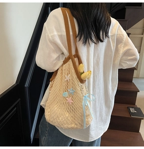 Detail of beige mesh tote bag with starfish charms and blue ribbon on a model