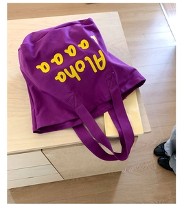 Detail of purple canvas tote bag with yellow Aloha print on light wood surface