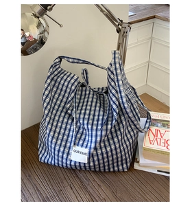Detail of blue and white gingham canvas tote bag with woven label on wooden table