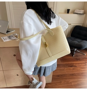 Detail showing cream tote bag with crocodile pattern and golden metal lock hardware
