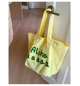 Detail of light yellow canvas tote bag with green Aloha print hanging on door