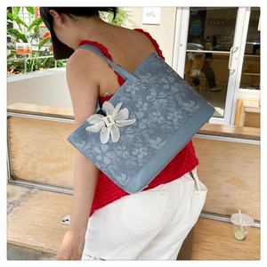 Close-up of blue floral tote bag with a large white 3D flower detail and thin shoulder straps