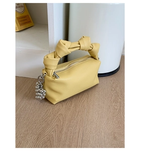Detail of yellow pleated handbag with twisted handle and silver bead charm