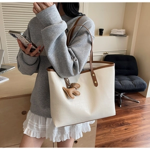 Detail of cream leather tote bag with brown handles and a cute dog charm in an office setting