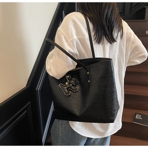 Detail of black crocodile embossed tote bag with a soft animal charm on a shoulder