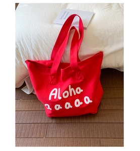 Detail view of the red canvas tote bag with white Aloha printing on a white bed surface