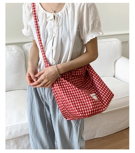 Detail of red gingham canvas tote bag with textured brand tag on shoulder of model