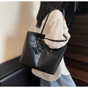 Detail of black crocodile texture tote bag with long shoulder strap and poodle charm