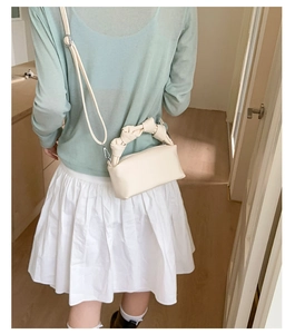 Detail of a creamy white handbag with knotted handle and detachable shoulder strap on model