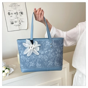 Detail of light blue floral tote bag with a white flower charm and brand tag