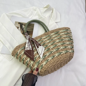 Detail of woven straw tote bag with green handles and floral scarf on white fabric