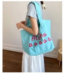 Detail view of light blue canvas tote bag featuring pink Aloha text worn by a model