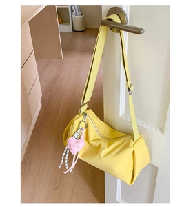 Détail du sac bandoulière en nylon jaune vif avec pendentif cœur rose sur une porte blanche