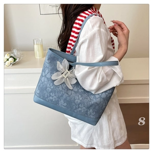 Detail of blue floral tote bag with white flower charm and textured fabric finish