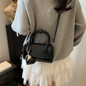 Close-up of black patent leather handbag with metal heart charm and crossbody strap