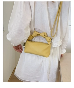 Detail of yellow pleated top handle bag with knot strap and decorative pearl charm