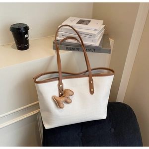 Detail view of white crocodile pattern tote bag with brown handles and a puppy charm