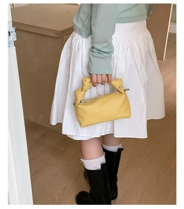 Detail of a bright yellow small square handbag with unique double knot handles for women