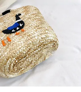 Detail view of woven straw bag texture with colorful bird embroidery and artisanal craftsmanship
