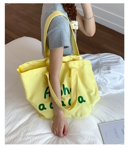 Detail of yellow canvas tote bag with green Aloha print worn by a model in a casual setting