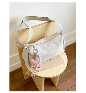 Detail of cream nylon crossbody bag with pink heart charm and braided rope zipper pull