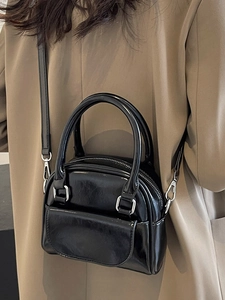 Elegant black patent leather handbag with round handles and crossbody strap on model