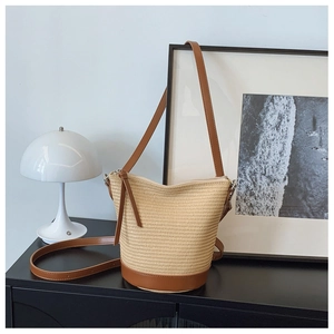 Détail du sac seau en paille tressée montrant la texture et la bandoulière en cuir brun