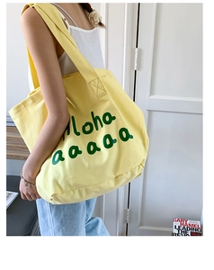 Detail view of large yellow canvas tote bag with green script lettering and cross-body strap