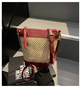 Detail of straw bucket bag with burgundy faux leather trim and golden zipper