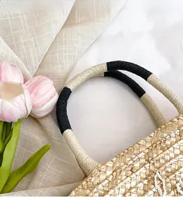 Detail of hand-woven straw bag featuring black and white cord-wrapped handle with tulips