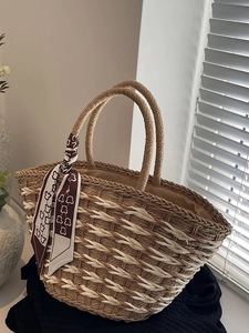 Handwoven straw tote bag with brown handles and decorative silk scarf for summer beach