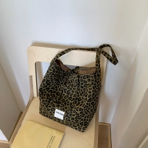 Detail of leopard print canvas tote bag with 'OUR FAVE' label on minimalist wooden chair