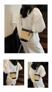 Detail view of woven straw crossbody bag with black leather trim and gold metal buckles