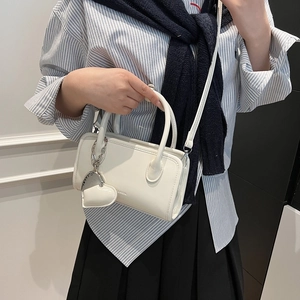 Detail shot of a cream PU leather bowling bag with heart charm and shoulder strap