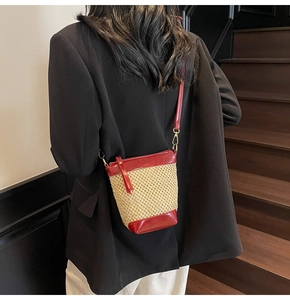 Detail view of woven straw bucket bag in red and beige with slim shoulder strap