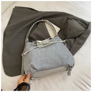 Detail der silbernen Plissee-Tasche mit Schleifen-Kordelzug auf grauem Blazer-Hintergrund