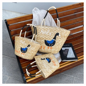 Detailed macro view of woven straw tote bags with goose embroidery on a wooden bench