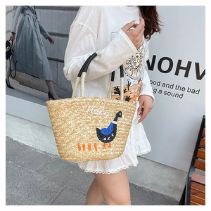Detail of handwoven straw tote featuring an embroidered blue swan and Hello lettering
