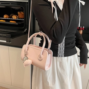 Detail view of light pink bowling handbag with heart charm and shoulder strap